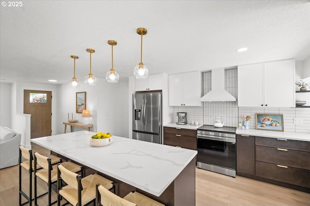kitchen with wall chimney range hood, stainless steel appliances, dark brown cabinets, white cabinetry, and recessed lighting
