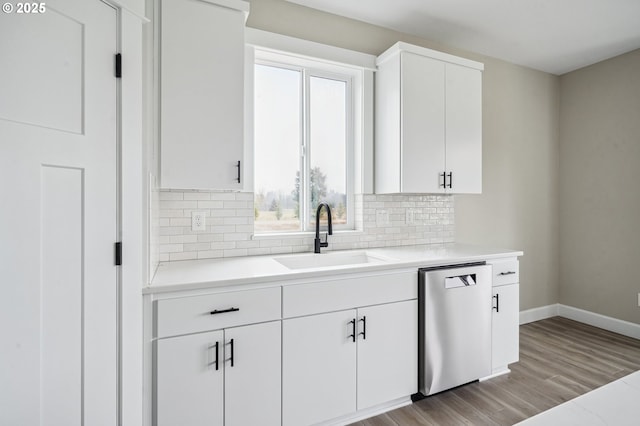 kitchen with sink, stainless steel dishwasher, white cabinets, light hardwood / wood-style floors, and backsplash