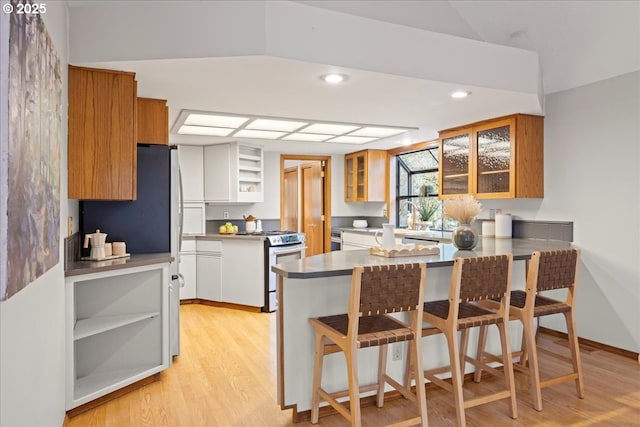 kitchen with stainless steel gas range, a breakfast bar, white cabinetry, kitchen peninsula, and light wood-type flooring