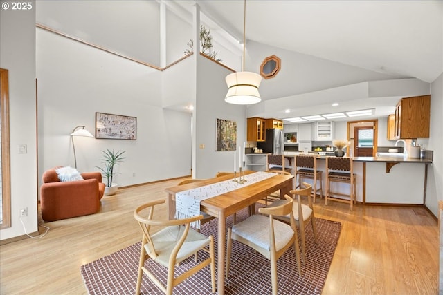 dining space with high vaulted ceiling and light hardwood / wood-style flooring