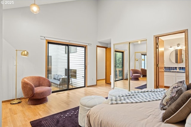 bedroom with access to exterior, a towering ceiling, ensuite bathroom, light hardwood / wood-style floors, and a closet