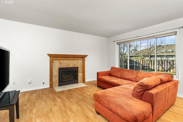 living room featuring a tiled fireplace, a textured ceiling, and light wood-type flooring