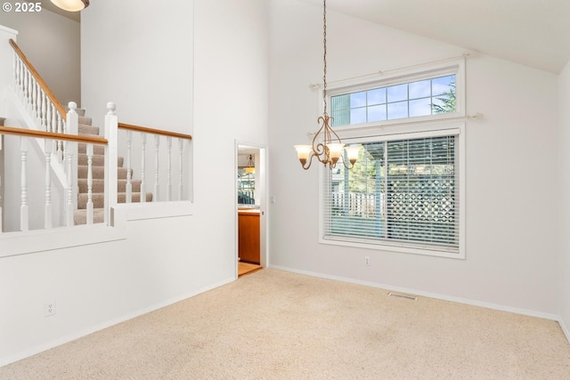 carpeted spare room featuring high vaulted ceiling and a chandelier