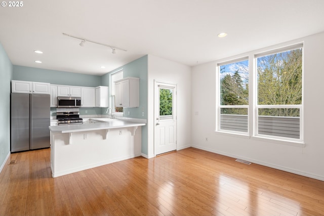 7408 SW Capitol Hwy, Portland, OR 97219 - kitchen featuring stainless steel appliances, track lighting, a peninsula, light countertops, and a kitchen breakfast bar