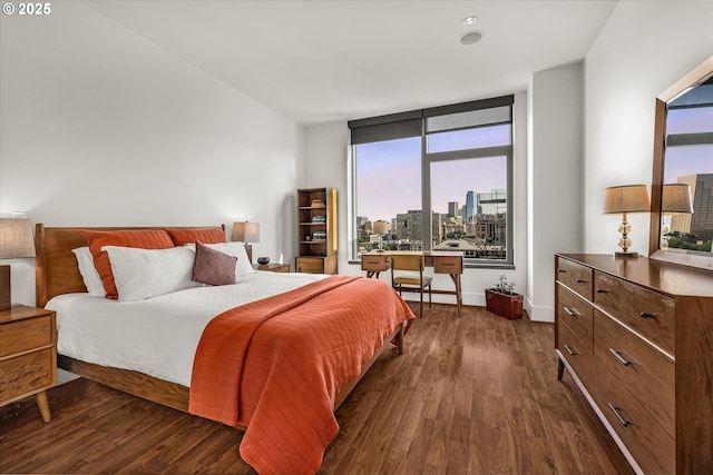 bedroom with dark wood-type flooring, a view of city, baseboards, and multiple windows