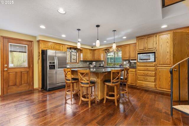 kitchen with stainless steel refrigerator with ice dispenser, white microwave, dark wood finished floors, and a kitchen island