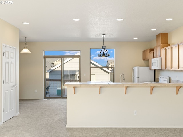 kitchen featuring a breakfast bar, decorative light fixtures, sink, light colored carpet, and white appliances