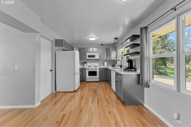 kitchen featuring white appliances, tasteful backsplash, gray cabinets, light countertops, and a sink