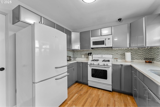 kitchen featuring white appliances, light wood-type flooring, decorative backsplash, and gray cabinetry