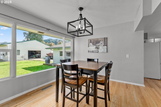 dining area featuring a notable chandelier, light wood-type flooring, visible vents, and baseboards