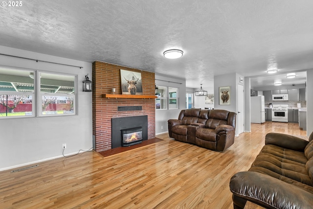 living area with a textured ceiling, a fireplace, visible vents, and light wood-style floors