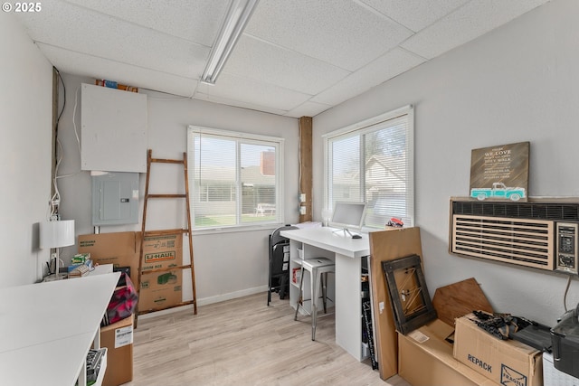 office featuring a paneled ceiling, light wood finished floors, electric panel, and baseboards