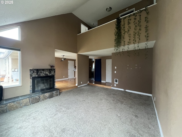 unfurnished living room with high vaulted ceiling, a stone fireplace, and carpet floors