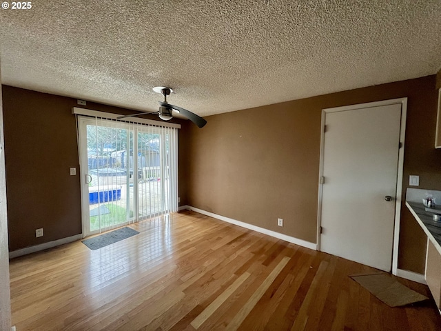 interior space featuring a ceiling fan, a textured ceiling, baseboards, and wood finished floors