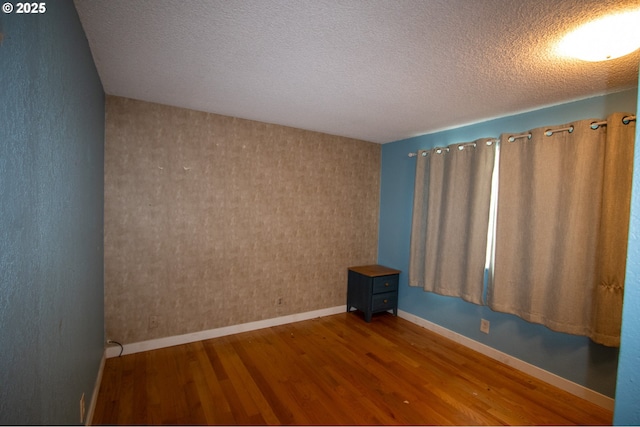 empty room featuring a textured ceiling, wood finished floors, and baseboards