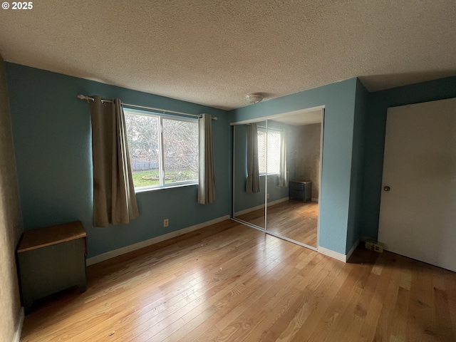 unfurnished bedroom with light wood-type flooring, a textured ceiling, baseboards, and a closet