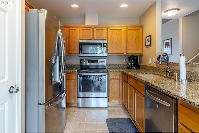 kitchen featuring light stone counters, light tile patterned flooring, a sink, appliances with stainless steel finishes, and brown cabinetry