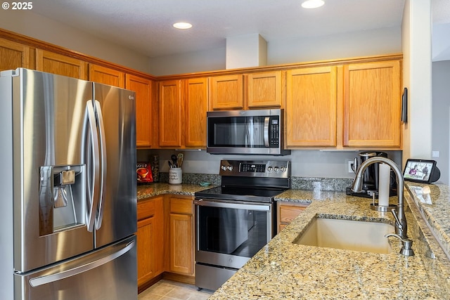 kitchen featuring appliances with stainless steel finishes, a sink, light stone counters, and recessed lighting