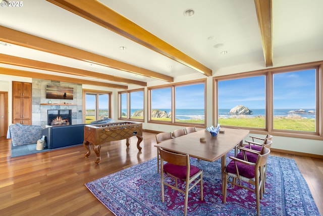 dining space featuring a water view, beamed ceiling, a healthy amount of sunlight, and wood finished floors