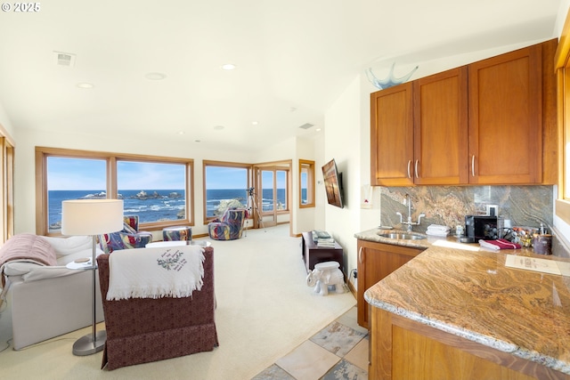kitchen featuring a sink, light stone countertops, backsplash, and brown cabinets