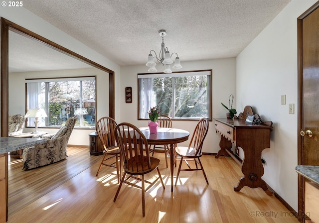 dining area featuring a notable chandelier, light wood-style flooring, a textured ceiling, and baseboards