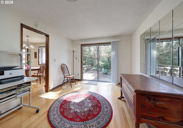 interior space featuring baseboards, a notable chandelier, light wood-style flooring, and a textured ceiling