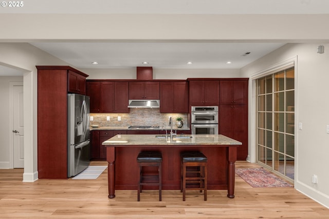 4661 Trillium, Woods, Lake Oswego, OR 97035 - kitchen with appliances with stainless steel finishes, under cabinet range hood, reddish brown cabinets, light wood-style flooring, and decorative backsplash