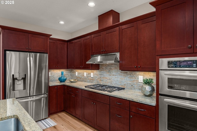 4661 Trillium, Woods, Lake Oswego, OR 97035 - kitchen featuring appliances with stainless steel finishes, under cabinet range hood, reddish brown cabinets, light stone countertops, and recessed lighting