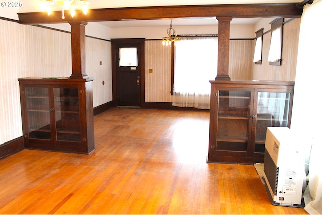 interior space with hardwood / wood-style floors, a notable chandelier, beamed ceiling, heating unit, and ornate columns