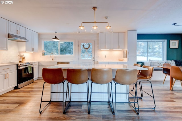 24492 SE Three Cedars St, Damascus, OR 97089 - kitchen featuring electric range, under cabinet range hood, white cabinets, backsplash, and a breakfast bar area