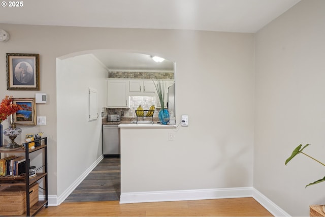 kitchen with white cabinetry, stainless steel dishwasher, wood-type flooring, and tasteful backsplash