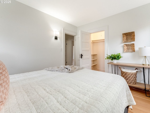 bedroom with a walk in closet and hardwood / wood-style floors