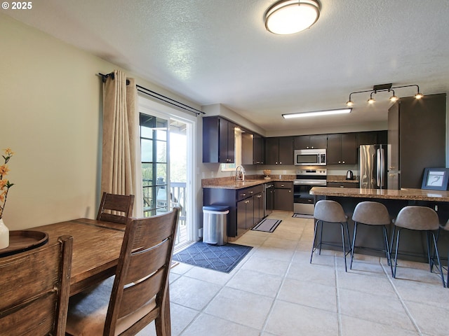 kitchen with a sink, appliances with stainless steel finishes, a kitchen bar, and a textured ceiling