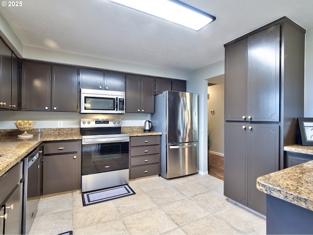 kitchen featuring appliances with stainless steel finishes, baseboards, and light stone counters