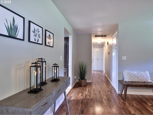 hall with a textured ceiling, baseboards, wood finished floors, and visible vents