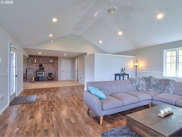 living area featuring a wood stove, visible vents, wood finished floors, and lofted ceiling