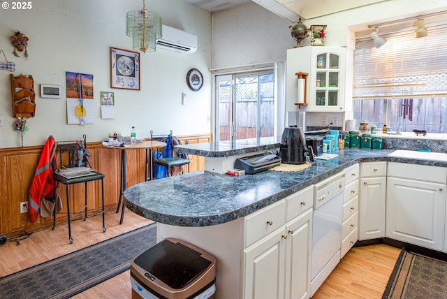 kitchen with white cabinetry, white dishwasher, kitchen peninsula, light hardwood / wood-style floors, and a wall unit AC