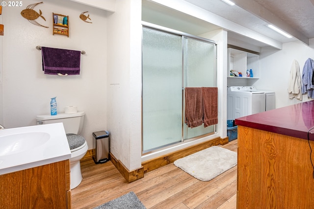 bathroom with hardwood / wood-style floors, a shower with shower door, vanity, toilet, and washing machine and dryer