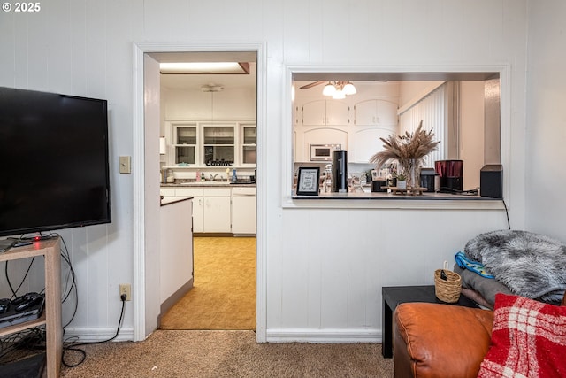 interior space featuring sink, white dishwasher, white cabinets, built in microwave, and light colored carpet