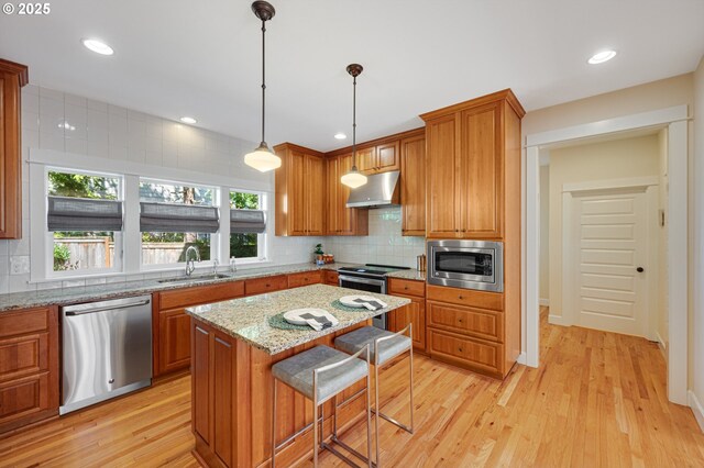 kitchen featuring appliances with stainless steel finishes, a sink, under cabinet range hood, tasteful backsplash, and light wood-type flooring