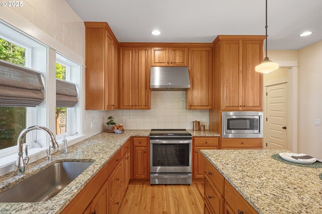 kitchen featuring appliances with stainless steel finishes, a sink, under cabinet range hood, light wood-style flooring, and brown cabinetry