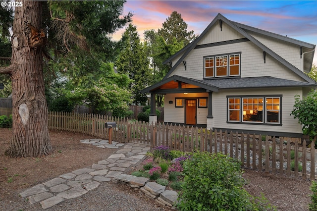 view of front facade with a porch, a fenced front yard, and roof with shingles