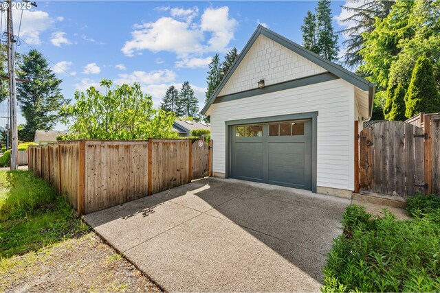 detached garage featuring concrete driveway and fence