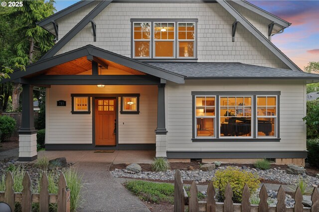 view of front of house featuring a shingled roof, fence, and a porch