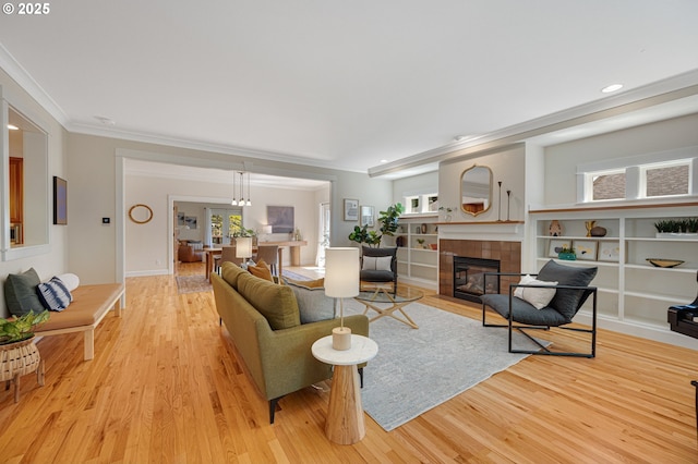 living room featuring ornamental molding, light wood-style floors, a tile fireplace, healthy amount of natural light, and recessed lighting