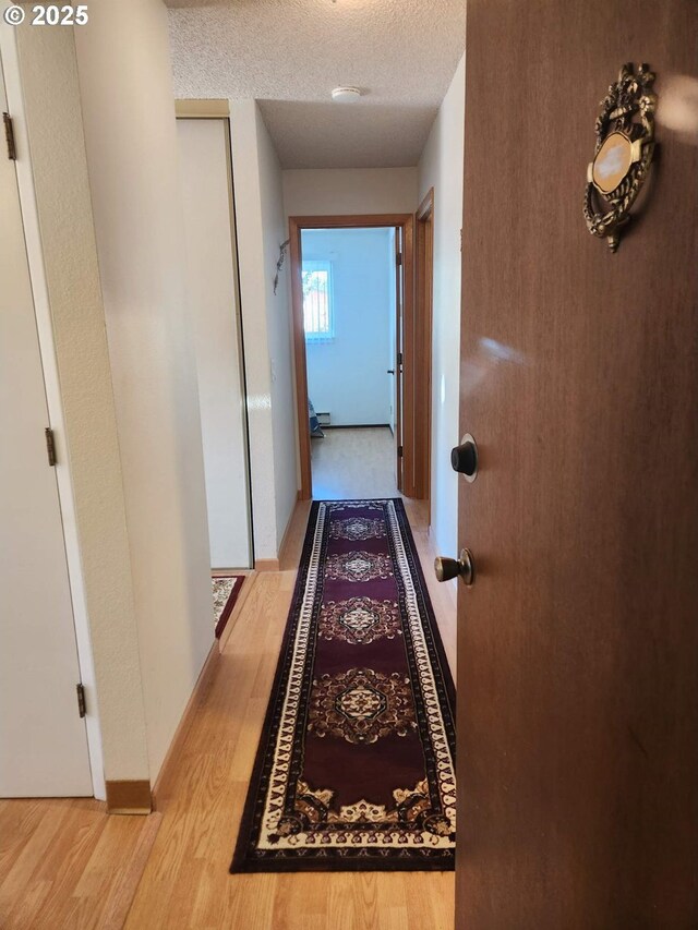 hall with a textured ceiling, light wood-style flooring, and baseboards