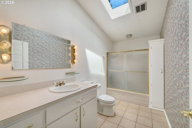 full bathroom with a skylight, tile patterned floors, bath / shower combo with glass door, toilet, and vanity