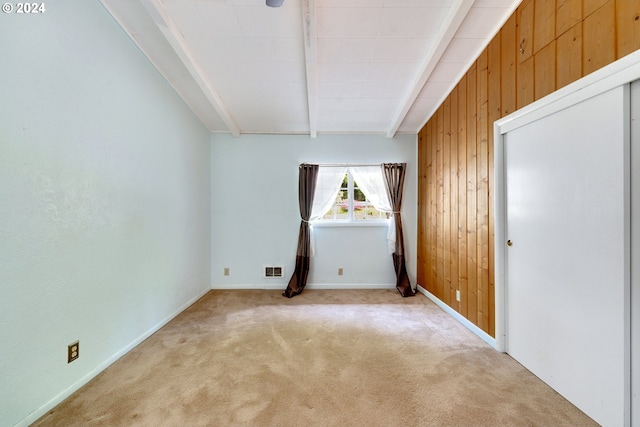 empty room featuring wooden walls, beamed ceiling, and light carpet