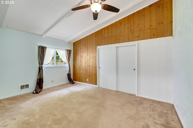 unfurnished bedroom with carpet, lofted ceiling with beams, ceiling fan, and wooden walls