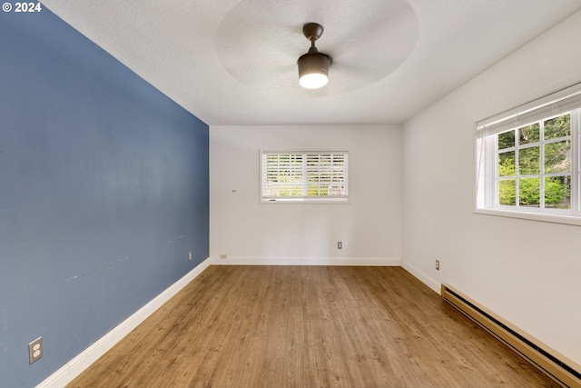 spare room featuring light wood-type flooring, plenty of natural light, ceiling fan, and a baseboard heating unit